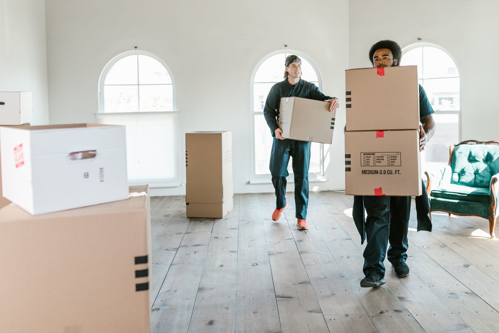 Two movers in uniform carrying boxes through a bright empty room