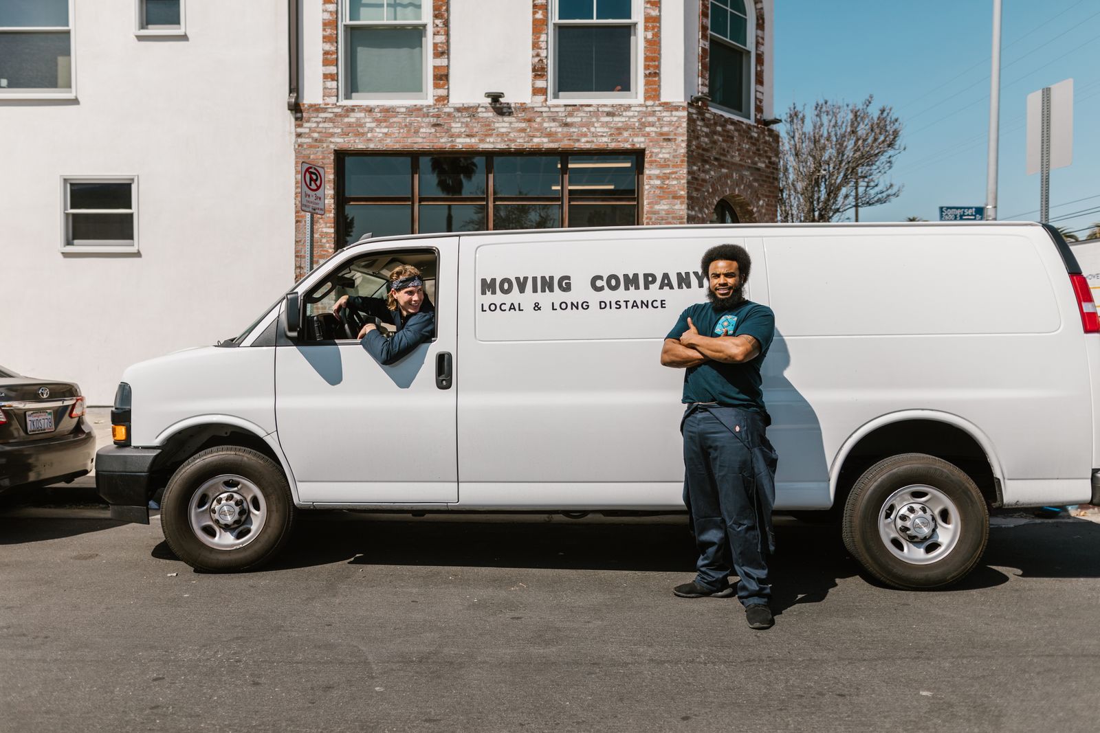 Mover smiling beside a white moving company van while a teammate sits at the wheel