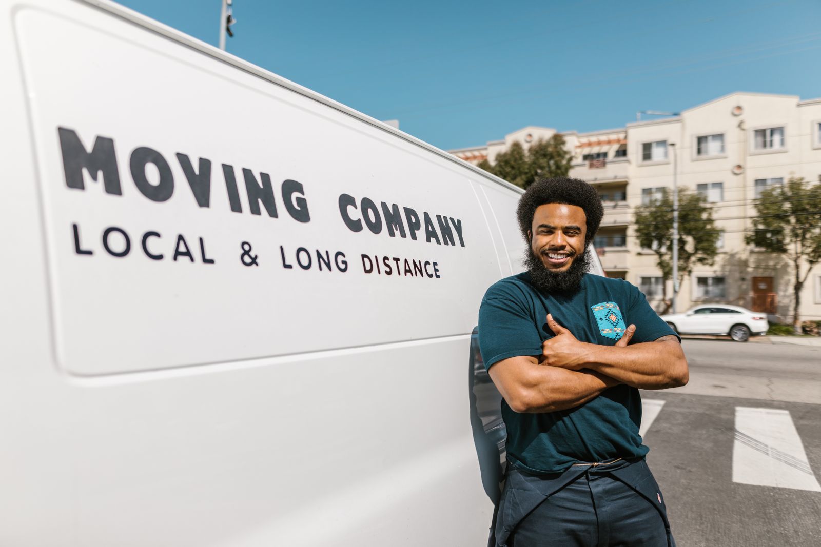 Smiling mover with arms crossed beside a moving van