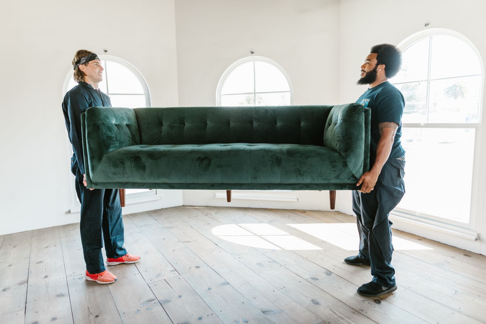 Two movers lifting a green sofa near arched windows