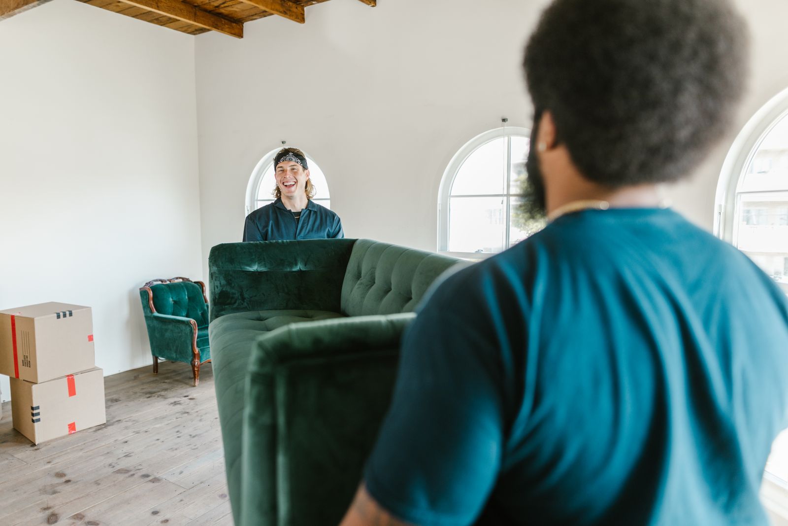Two movers carrying a green velvet couch in a bright room