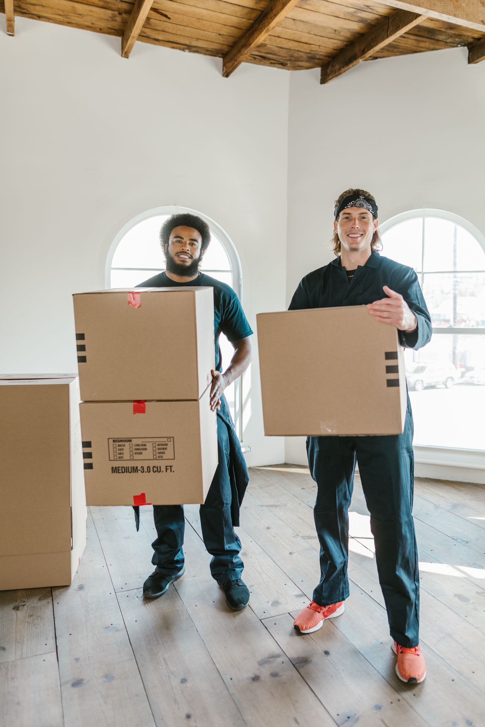 Two movers standing in a room holding stacked cardboard boxes